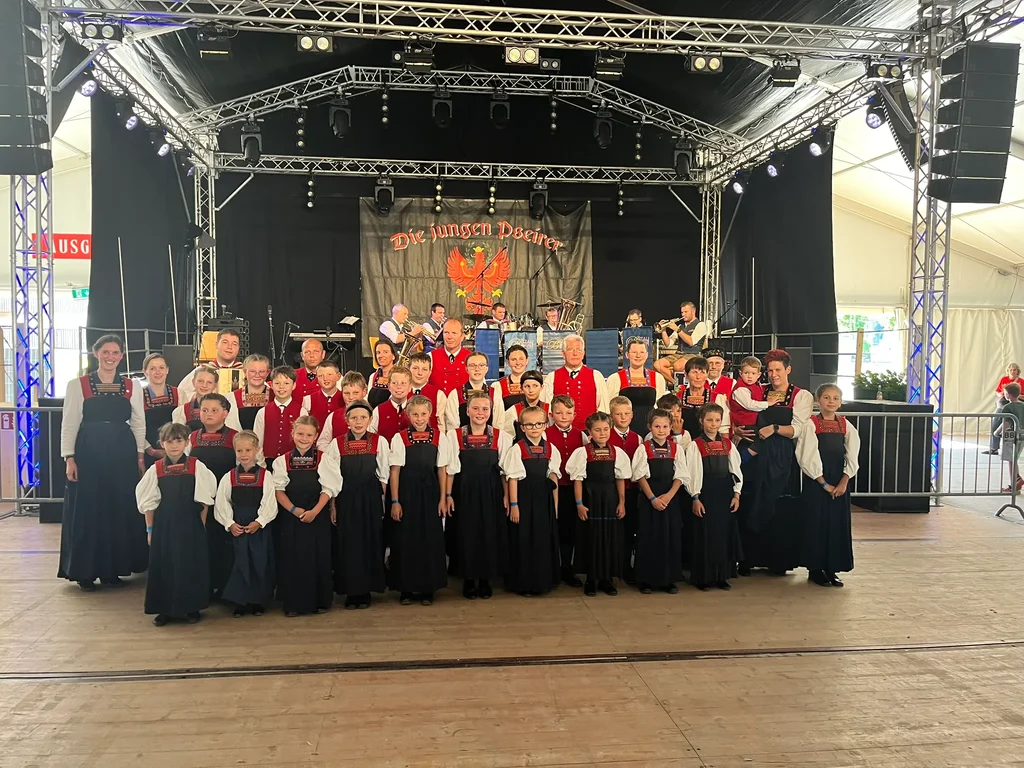 Die Kindertrachtengruppe und die Tanzgruppe Hittisau auf der Festbühne in Bezau, dahinter eine Musikkapelle
